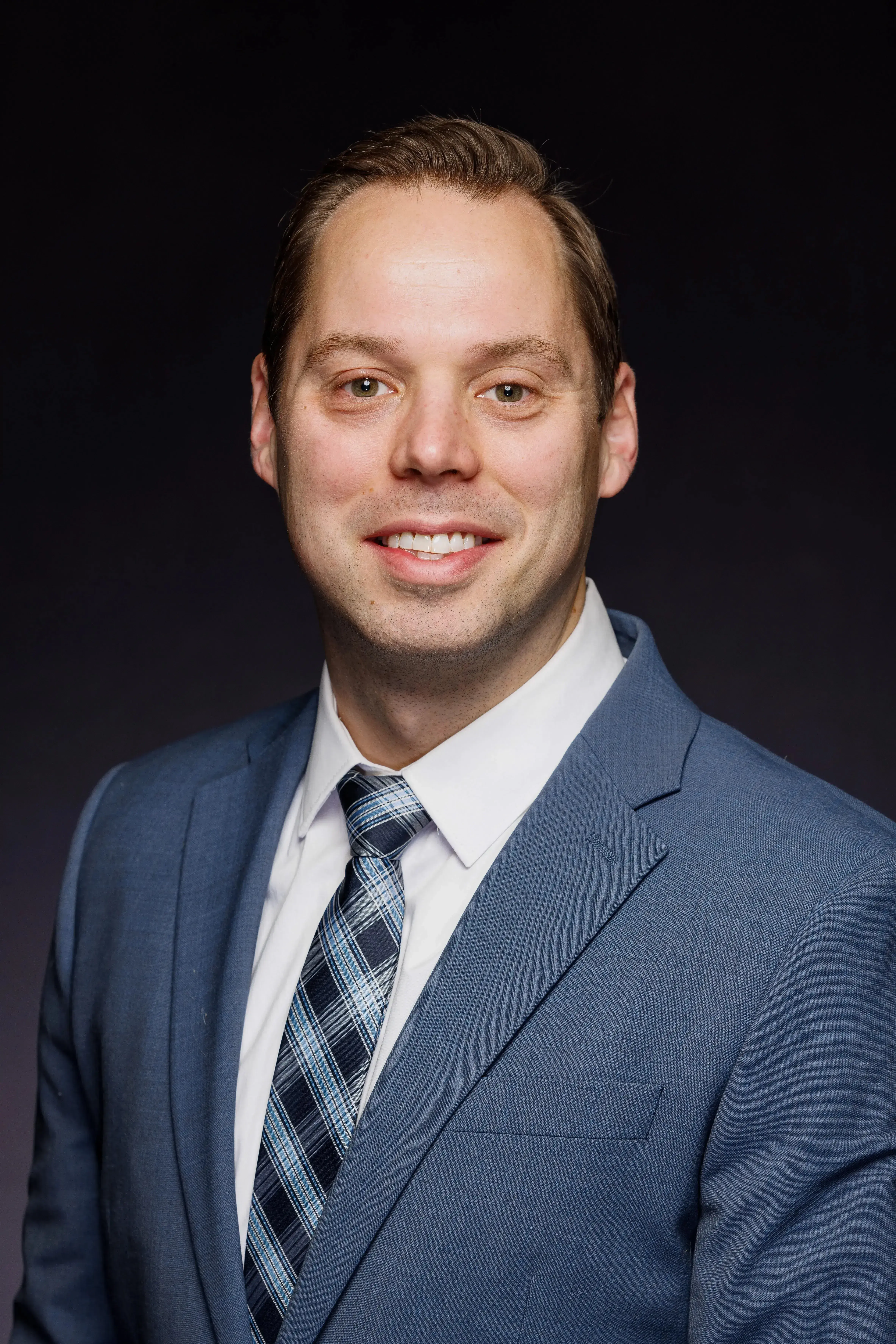 headshot of man wearing navy suit with blue patterned tie and white button down shirt