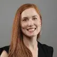 a woman with red hair posing for a headshot wearing a black blouse against a gray background