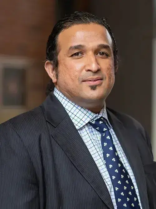 headshot of man in dark gray suit with a dark blue spotted tie and blue and white plaid button down