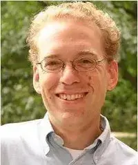 headshot of man in glasses and light blue button down against greenery and leaves
