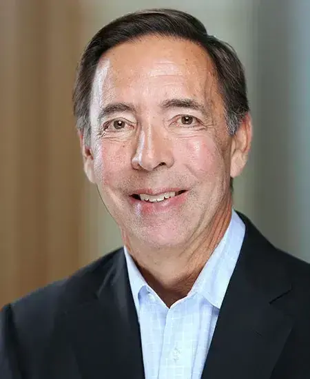 Jon Chait posing for a headshot wearing a light blue button down and black blazer.