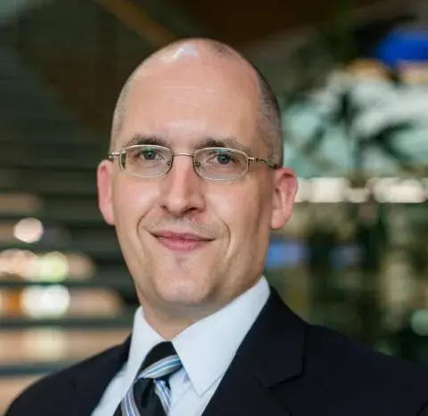 Nathan Vanderford posing for headshot, wearing a black suit and tie and glasses